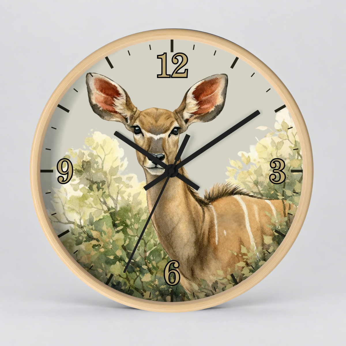 A round wall clock with a light wood frame featuring a printed illustration of a deer among green foliage on the clock face, with black hands and gold Arabic numerals, shown against a light gray background.