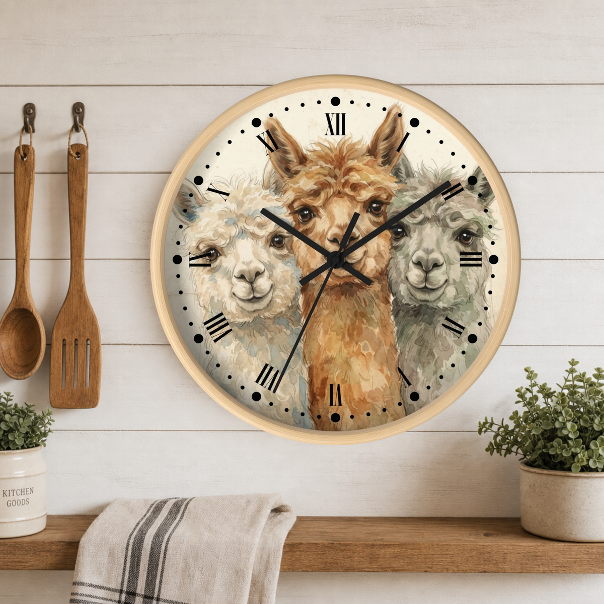 Round wall clock with a light wood frame featuring three alpaca illustrations on the clock face, mounted on a white wood paneled wall above a wooden shelf with kitchen utensils and plants.