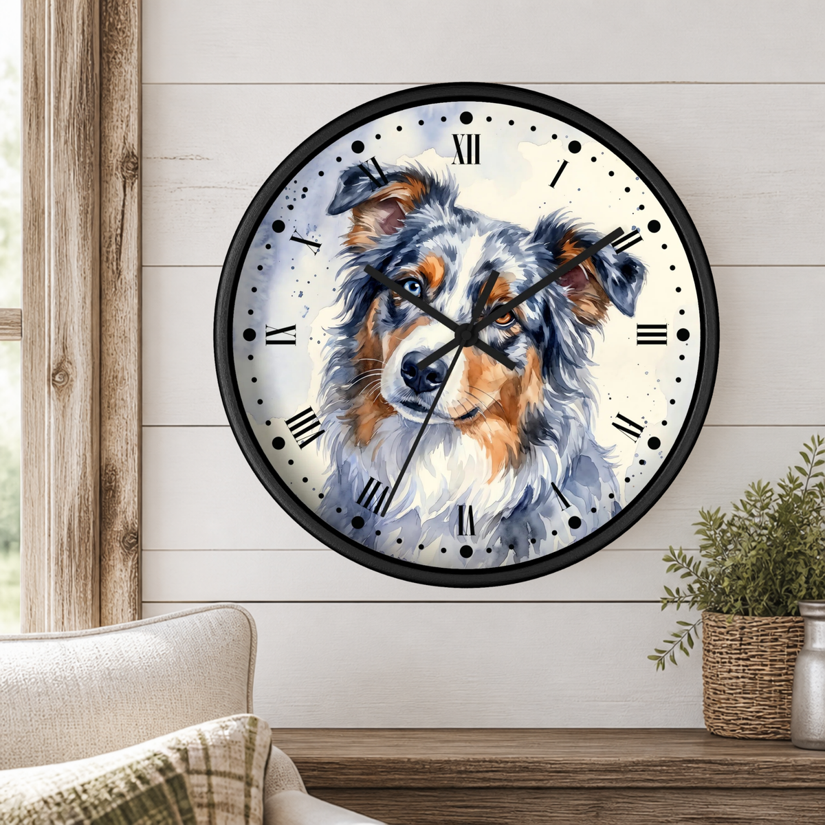 A round wall clock with a black frame and a watercolor-style dog portrait on the face, mounted on a white shiplap wall above a wooden table with a plant and part of a chair visible.