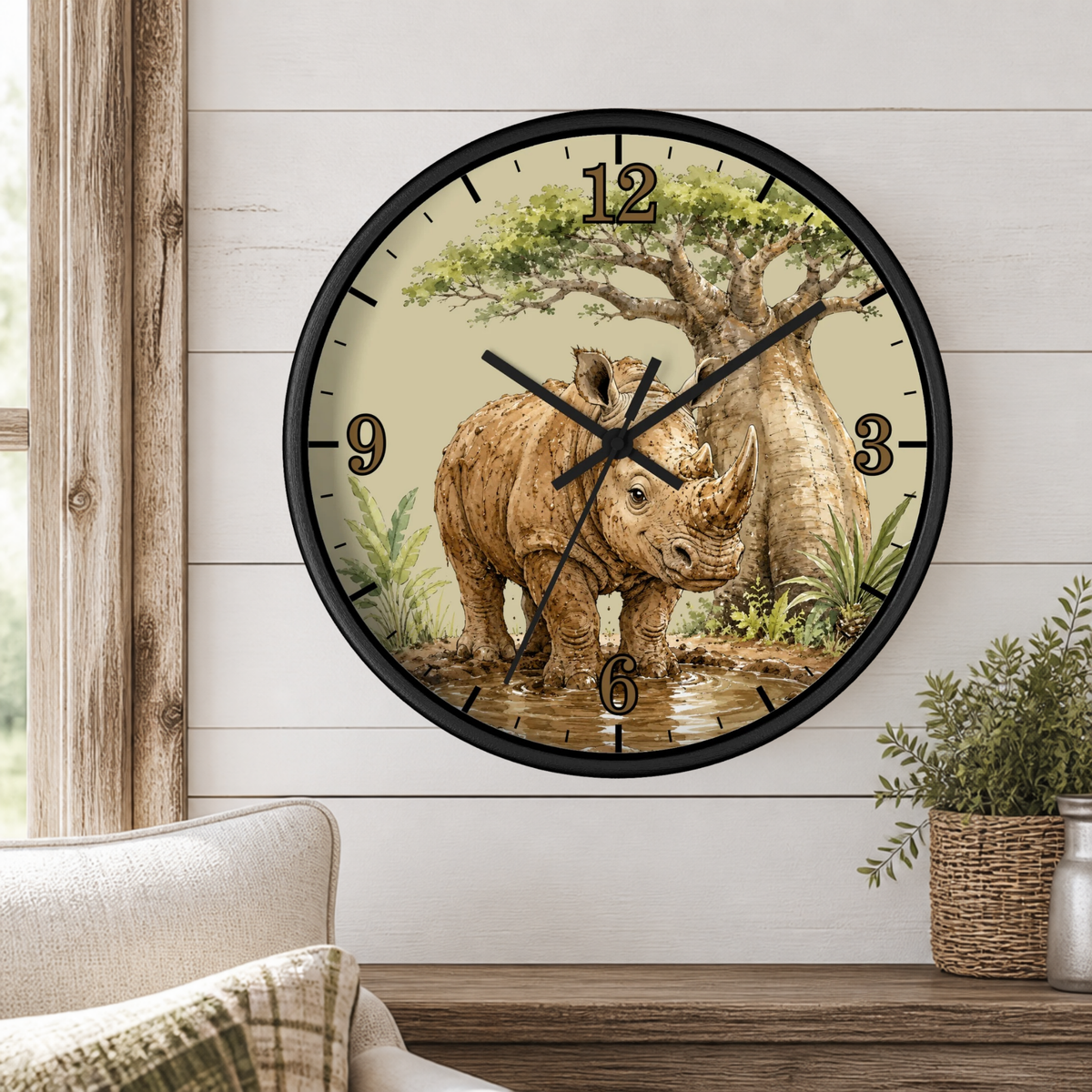 A round wall clock with a black frame and a safari-themed illustration of a rhinoceros under a tree, mounted on a white shiplap wall above a wooden console table with a plant and part of a sofa visible.