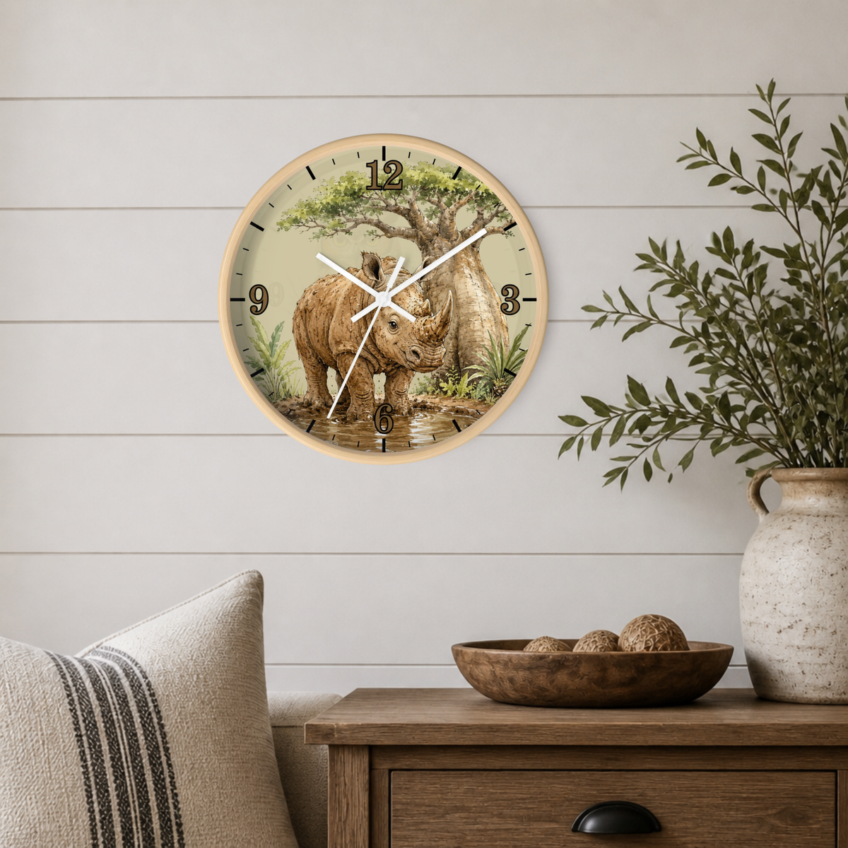A round wall clock with a light wood frame hangs on a white shiplap wall above a wooden side table. The clock face features an illustration of a rhinoceros under a tree.