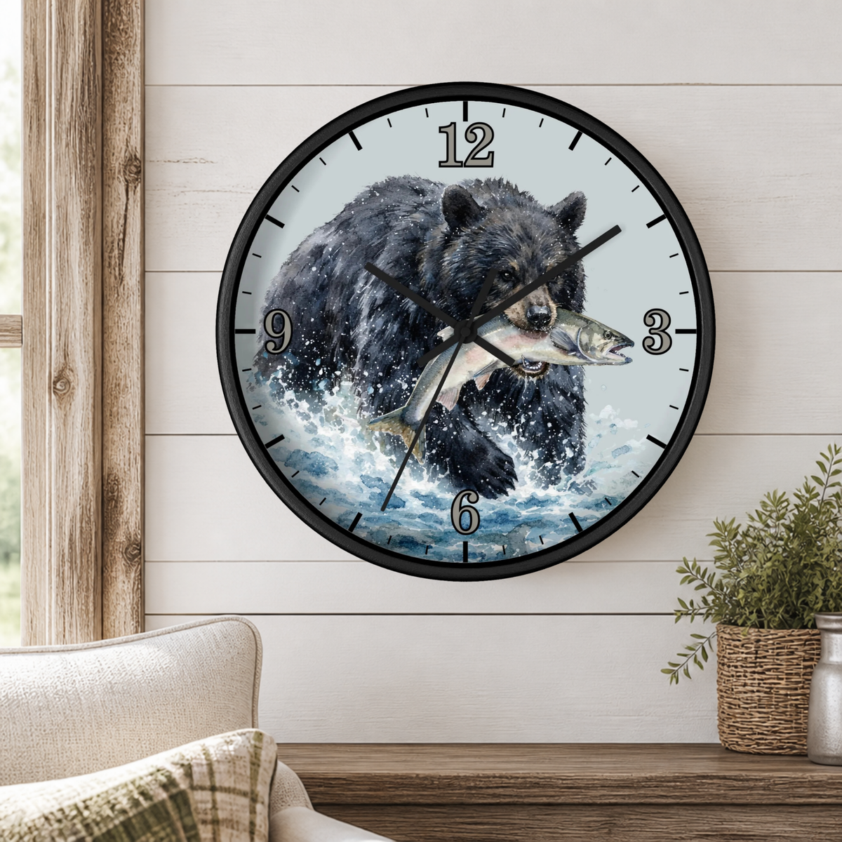 A round wall clock with a black bear and fish illustration, mounted on a white shiplap wall above a wooden mantel with a plant and part of a sofa visible.