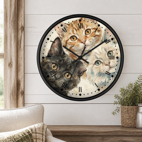 Round wall clock with a black frame and Roman numerals, featuring a watercolor-style illustration of three cats on the clock face, mounted on a white shiplap wall above a wooden mantel with a plant.