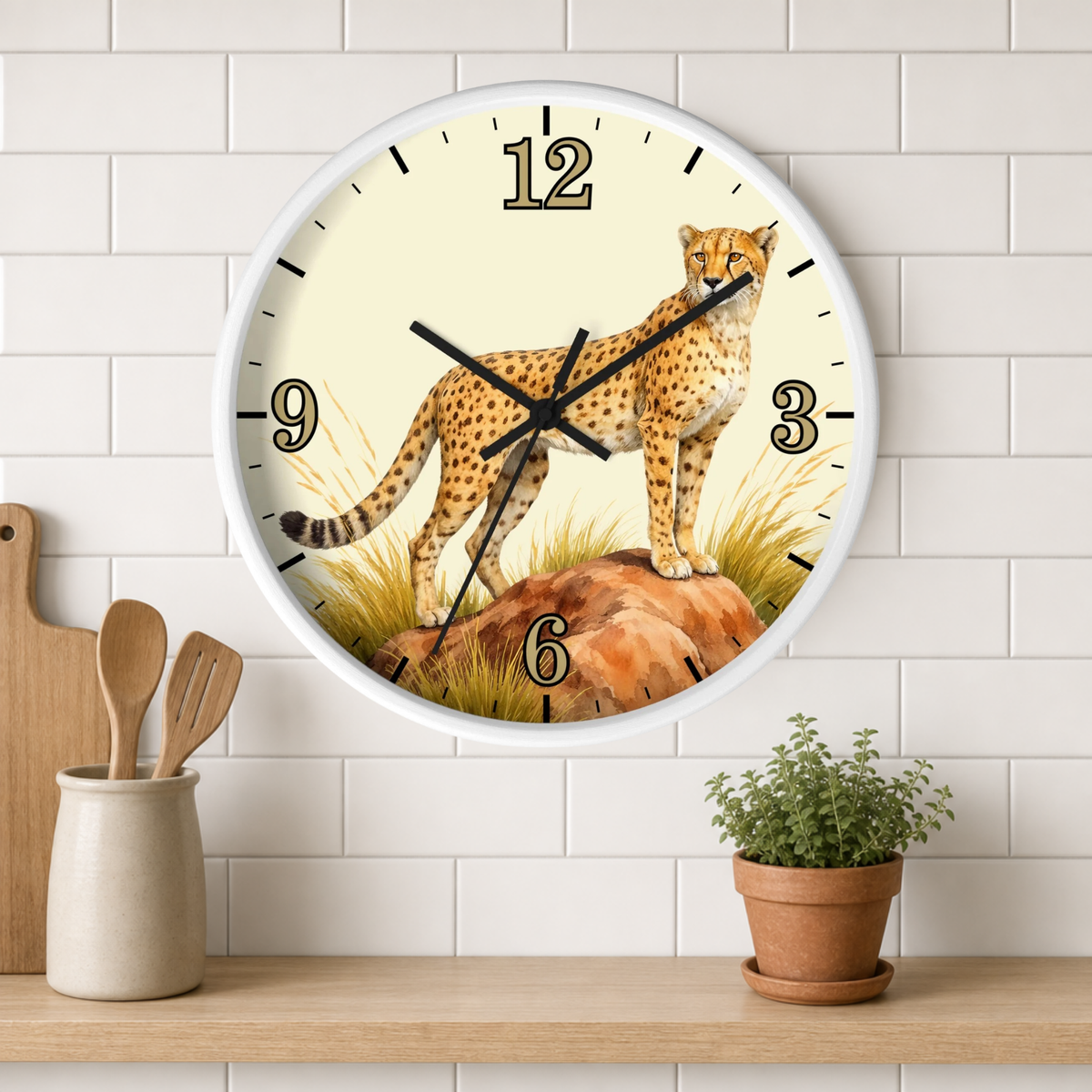 A round wall clock with a white frame hangs on a white subway-tile wall above a wooden shelf. The clock face features a detailed illustration of a cheetah standing on rocks with dry grass, set against a cream background.