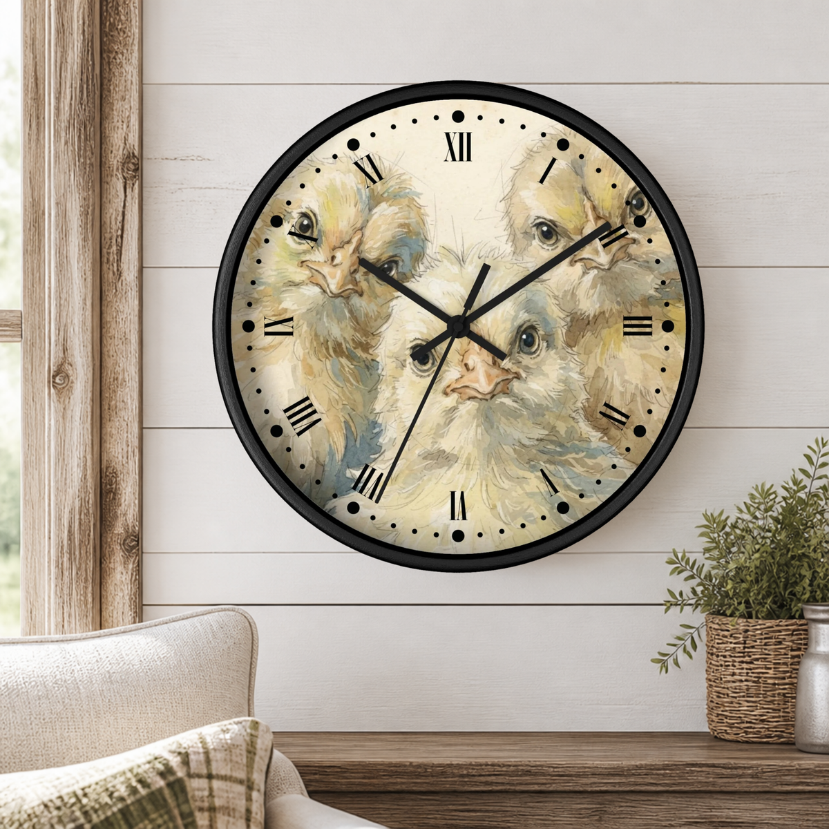 A round wall clock with a black frame and a vintage-style illustration of three yellow chicks on the face, mounted on a white shiplap wall above a wooden shelf with a small potted plant.
