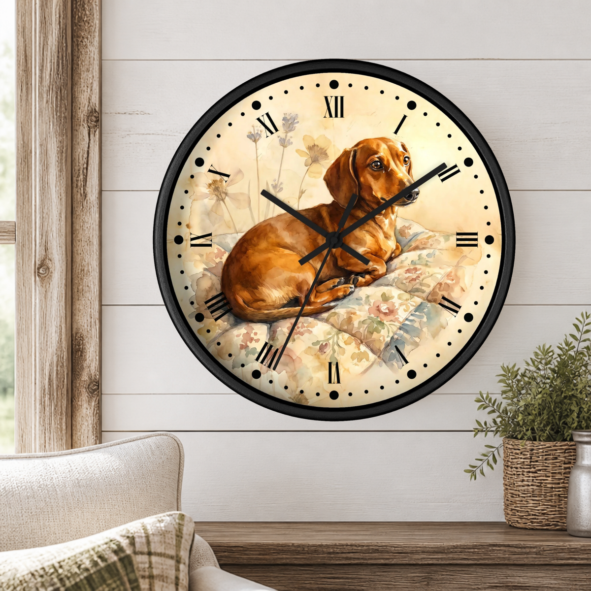 A round wall clock with a black frame and a vintage-style illustration of a brown dachshund lying on a floral blanket, mounted on a white shiplap wall above a wooden table with a plant.