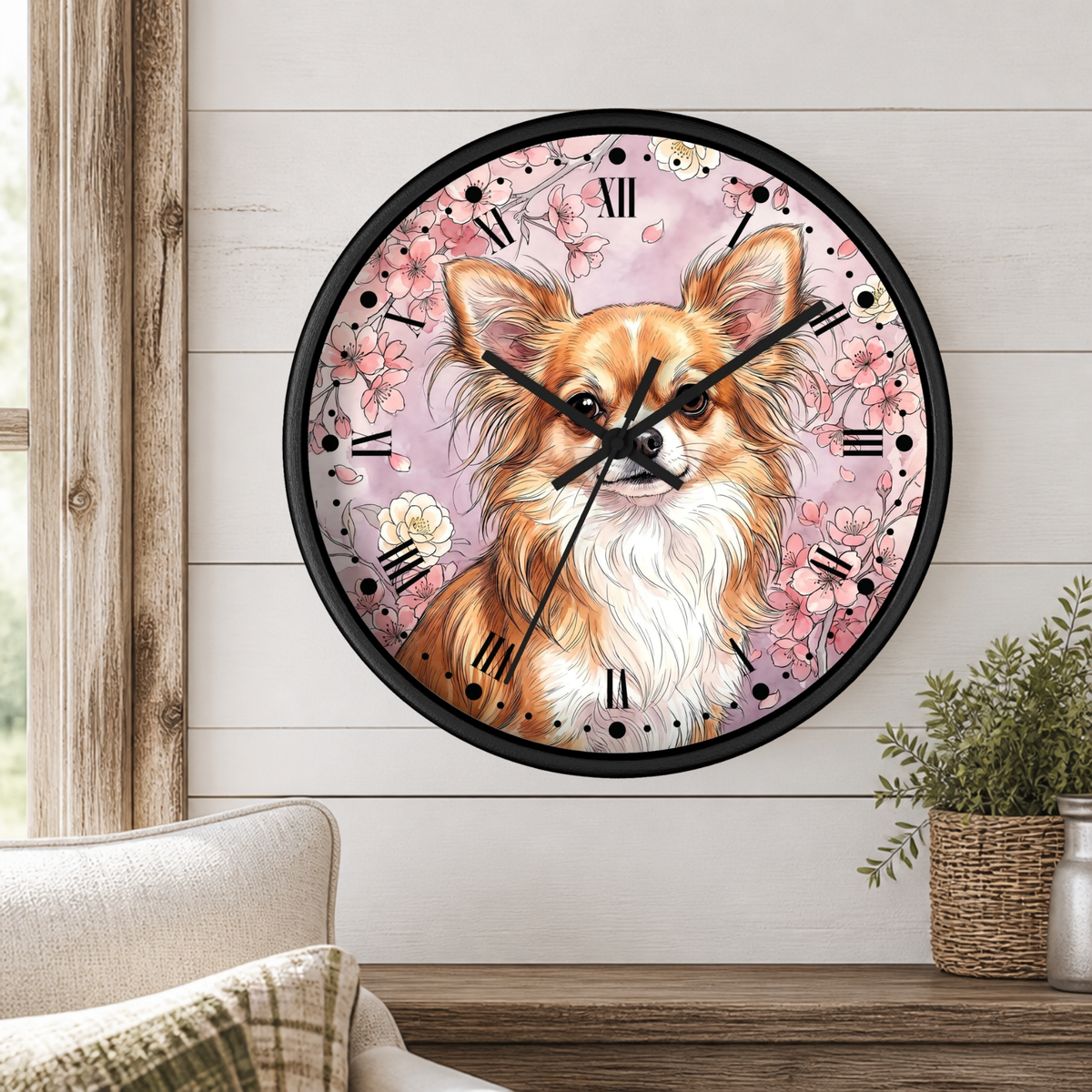 A round wall clock with a black frame and a printed illustration of a fluffy tan and white dog on a pink floral background, mounted on a white paneled wall above a wooden table with a plant and part of a chair visible.