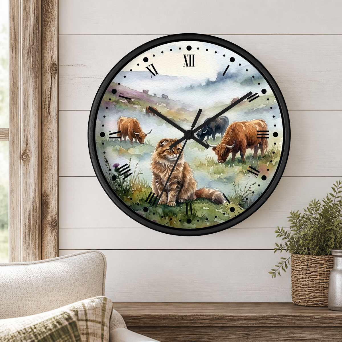 A round wall clock with a black frame and a printed illustration of Highland cattle in a grassy field, mounted on a white shiplap wall above a wooden table with a plant and part of a sofa visible.