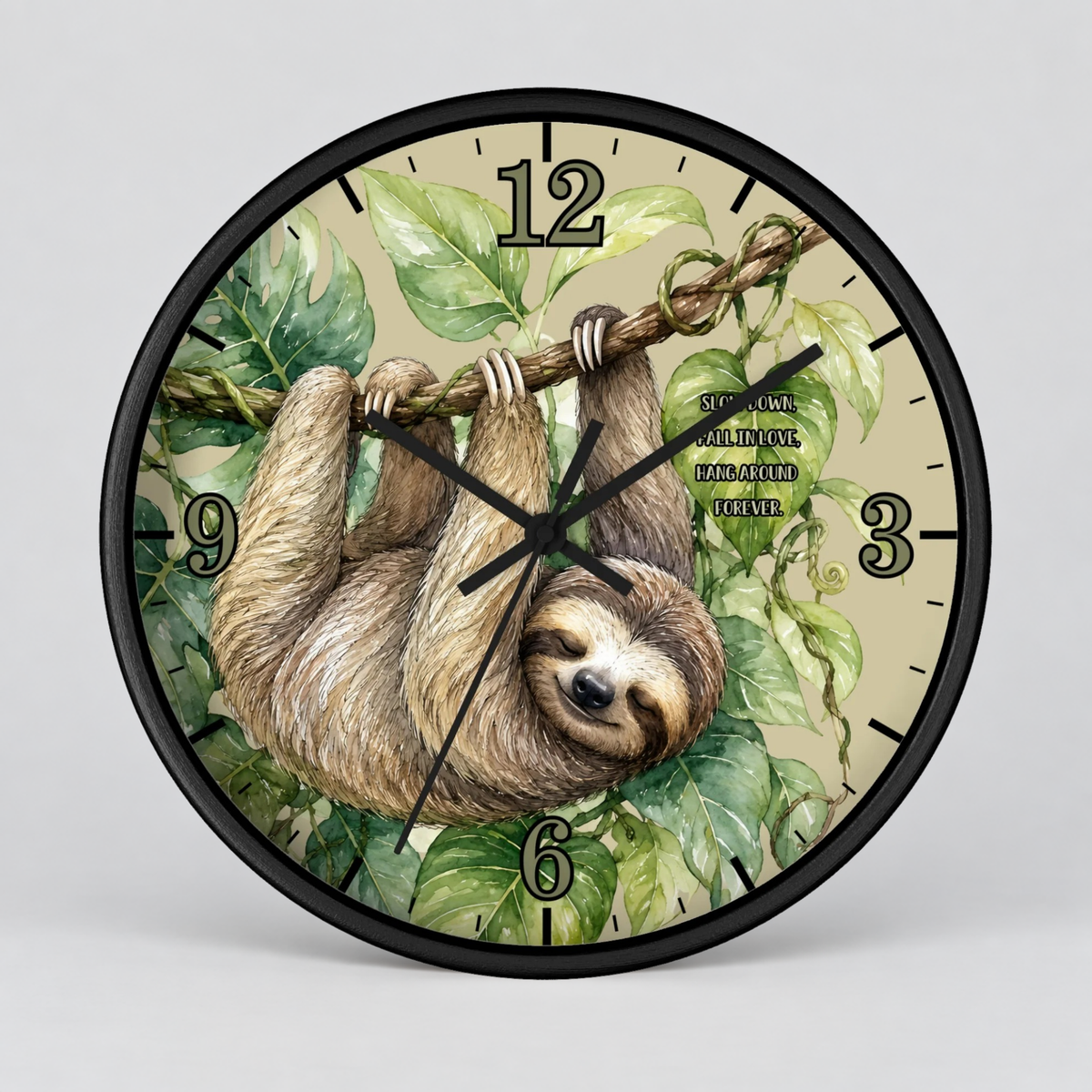 A round wall clock with a black frame and a printed illustration of a sloth hanging from a tree branch among green leaves on a light beige background. The clock has black Arabic numerals and black hands, photographed against a light gray studio background.