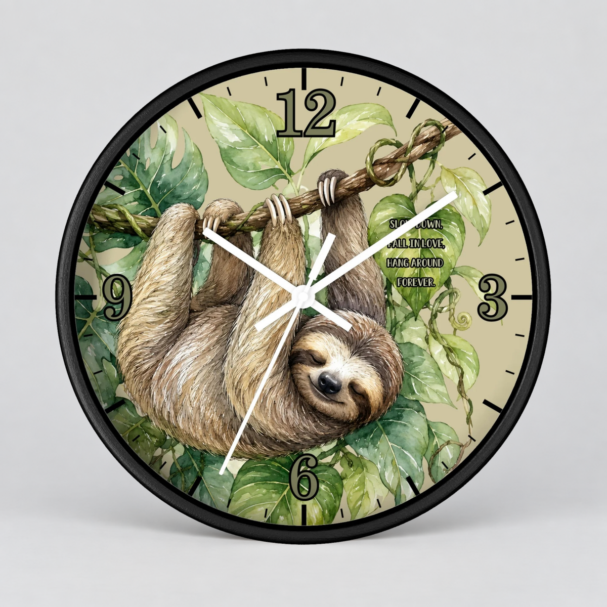 Round wall clock with a black frame and a printed illustration of a sloth hanging from a tree branch among green leaves on a light beige background. The clock face has black Arabic numerals and white hands, shown against a neutral light gray background.