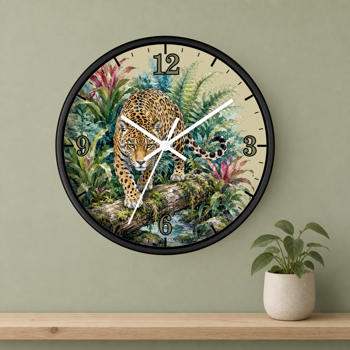 A round wall clock with a black frame and a tropical jungle illustration featuring a leopard, mounted on a sage green wall above a wooden shelf with a small potted plant.