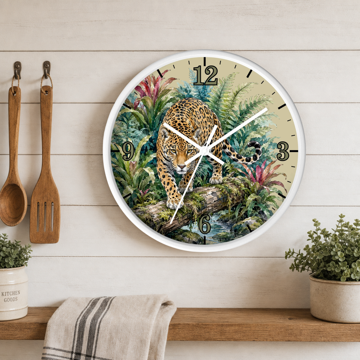 A round wall clock with a white frame hangs on a light wood plank kitchen wall above a wooden shelf. The clock face features a detailed illustration of a leopard walking through lush green and pink tropical foliage.