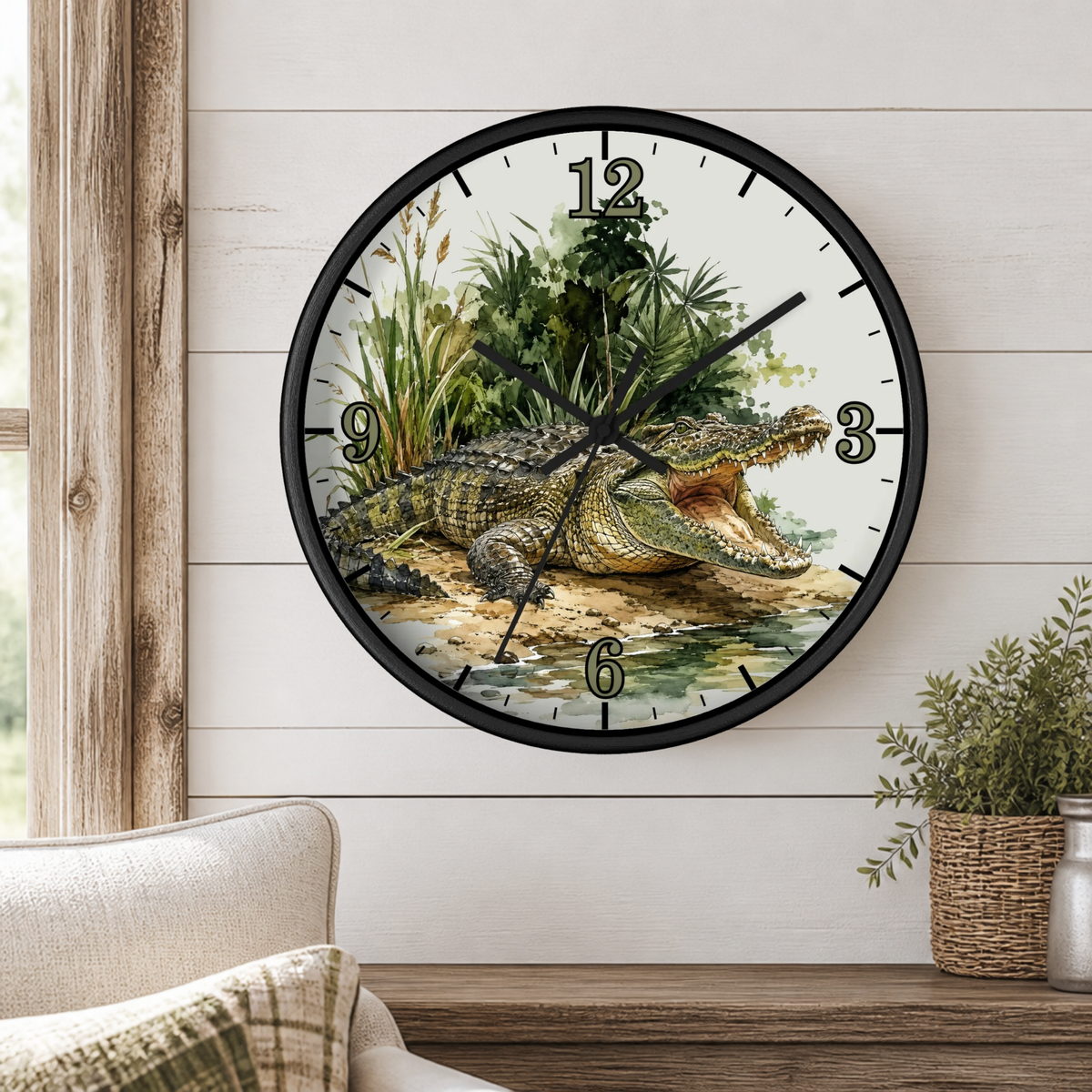 A round wall clock with a black frame and a tropical crocodile illustration on the face, mounted on a white wood-paneled wall above a wooden shelf with a plant and part of a sofa visible.