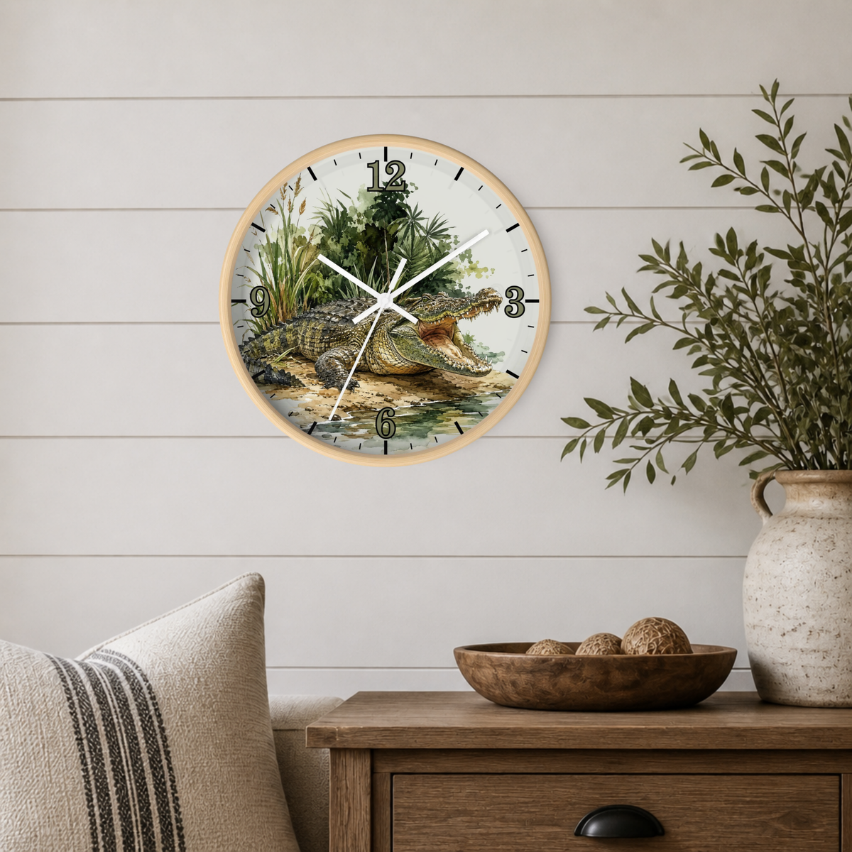 A round wall clock with a natural wood frame hangs on a white shiplap wall above a wooden side table. The clock face features a vintage-style illustration of an alligator in a swamp with palm trees.