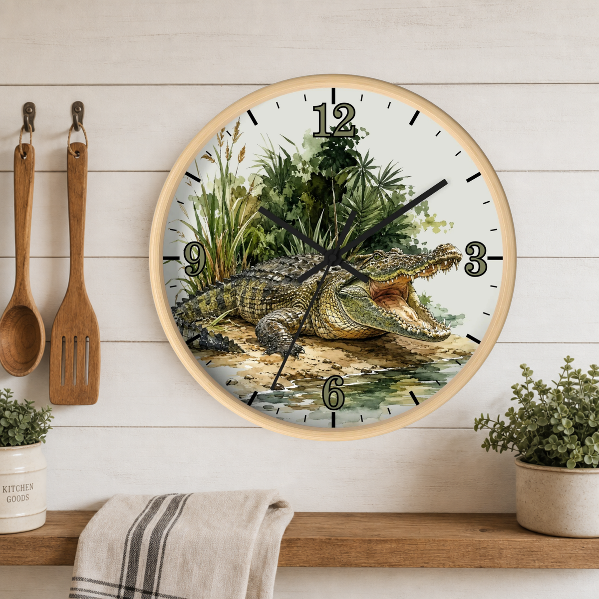 Round wall clock with a light wood frame featuring a detailed illustration of an alligator in a swampy landscape, mounted on a white wood paneled wall above a shelf with kitchen utensils and plants.