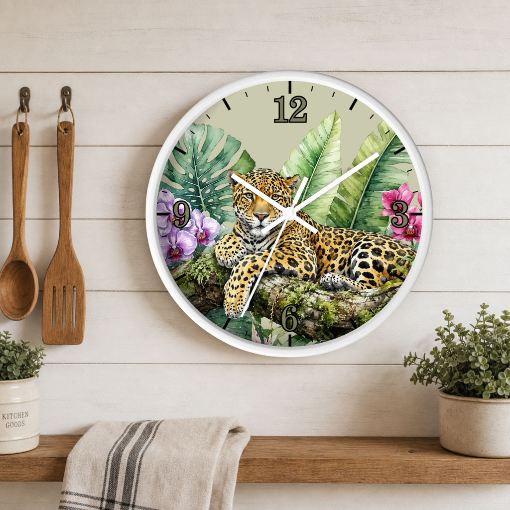 A round wall clock with a white frame hangs on a light wood plank kitchen wall above a wooden shelf. The clock face features a detailed illustration of a leopard resting among tropical green leaves and purple flowers, with black Arabic numerals.