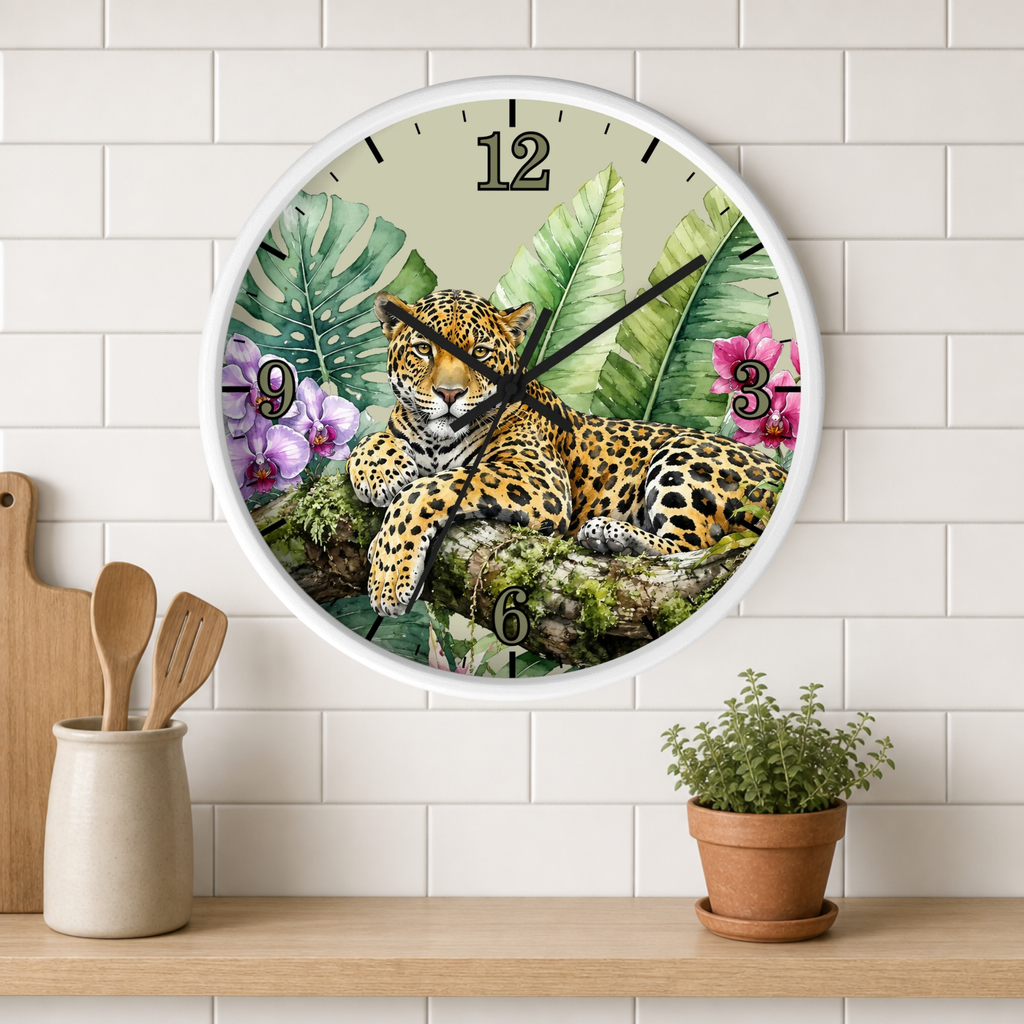 A round wall clock with a white frame hangs on a white subway-tile wall above a wooden shelf. The clock face features a detailed illustration of a leopard resting among green tropical leaves and pink flowers.