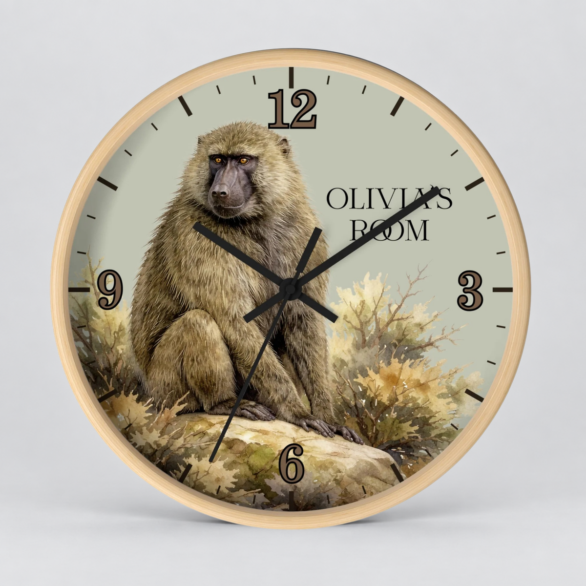 A round wall clock with a light wood frame and a printed dial featuring a baboon illustration, black numerals, and the text 'OLIVIA'S ROOM'.