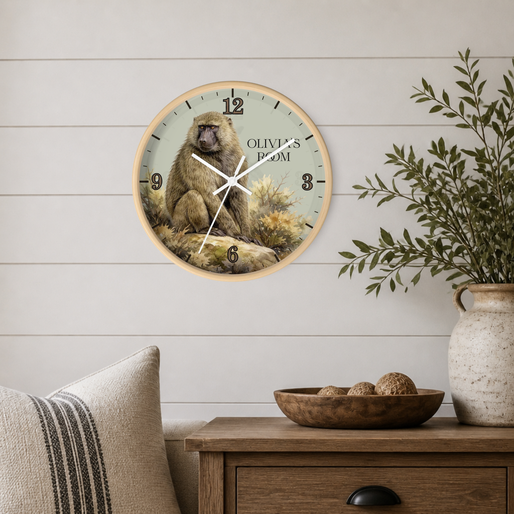 A round wall clock featuring a seated baboon illustration and the text 'OLIVIA'S ROOM', mounted on a white shiplap wall above a wooden side table with a vase and bowl.