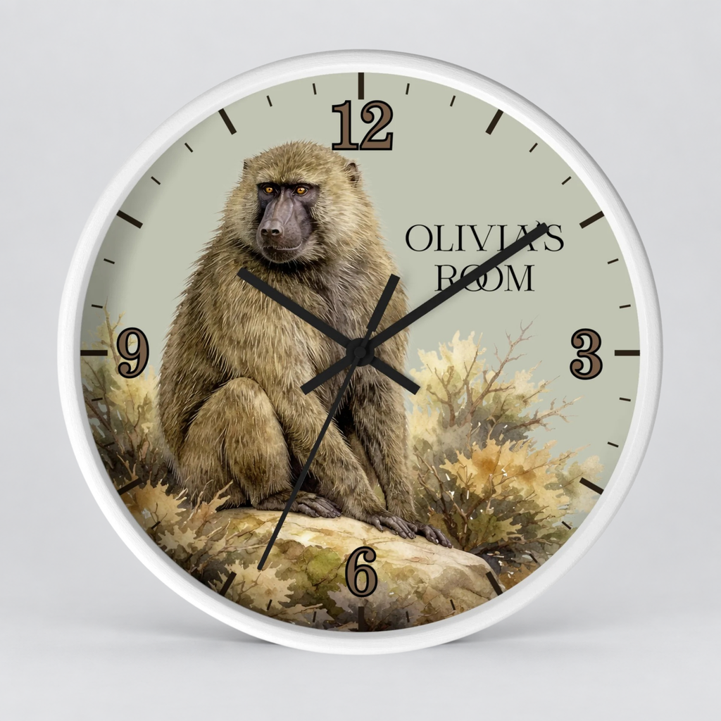 A round wall clock with a white frame and a printed face showing a baboon sitting on a rock, with the text 'OLIVIA'S ROOM' and black Arabic numerals. The clock is photographed against a light gray background.