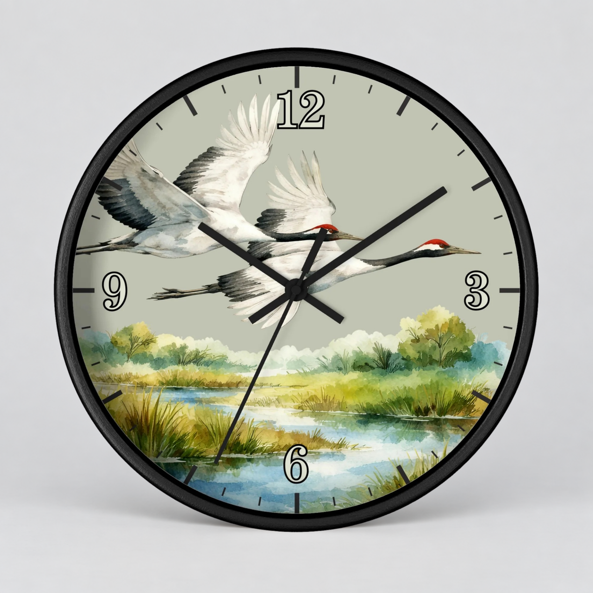 A round wall clock with a black frame and a printed nature scene on the face showing two flying cranes over a marsh landscape. The clock has black numerals and black hands on a light gray background.
