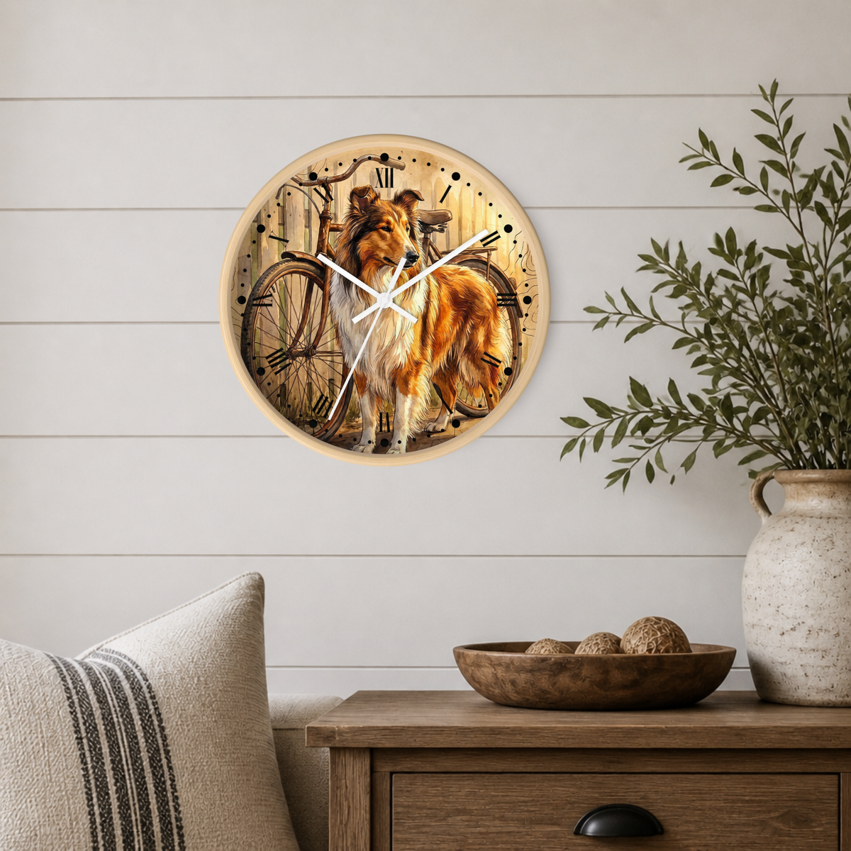 A round wall clock with a printed illustration of a collie dog and bicycle, mounted on a white shiplap wall above a wooden side table with a vase and bowl.