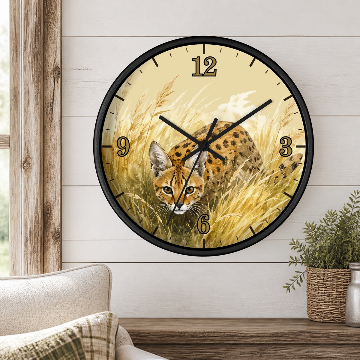 A round wall clock with a black frame and a printed design of a spotted big cat in tall golden grass, mounted on a white shiplap wall above a wooden shelf with a plant and part of a sofa visible.