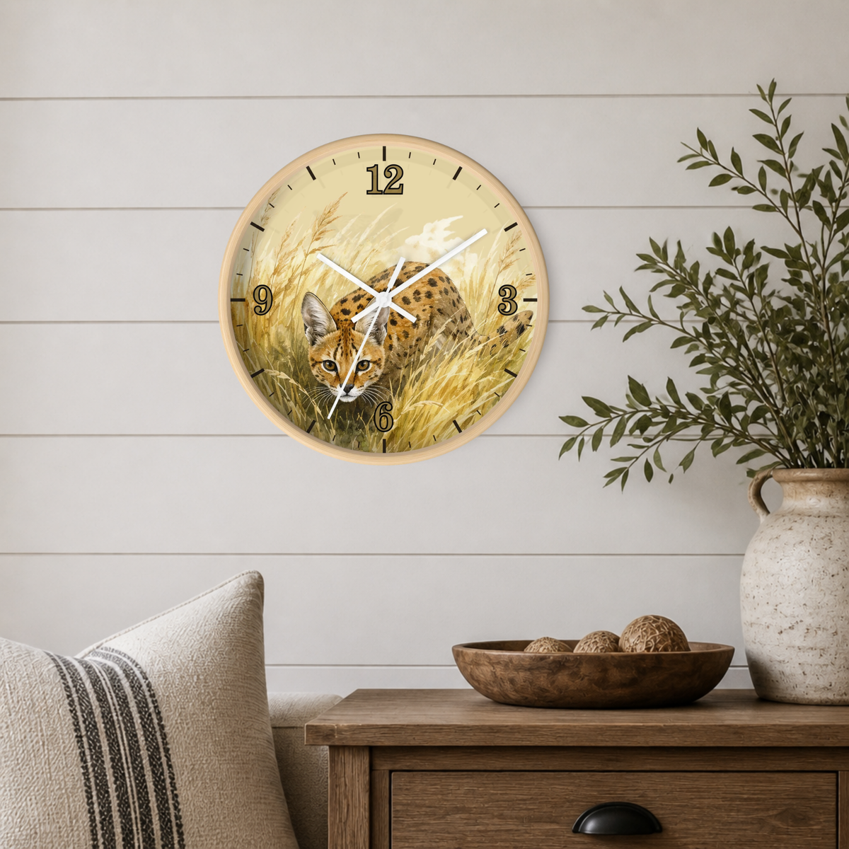 A round wall clock with a natural wood frame hangs on a white shiplap wall above a wooden side table. The clock face features a detailed illustration of a spotted big cat in golden grass.