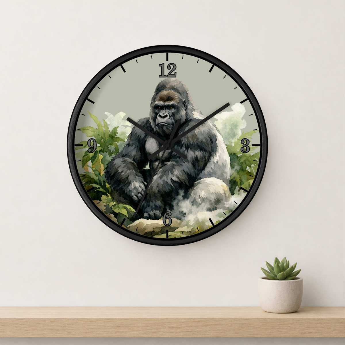 A round wall clock with a black frame and a printed illustration of a gorilla on the face, mounted on a light gray wall above a wooden shelf with a small potted succulent.
