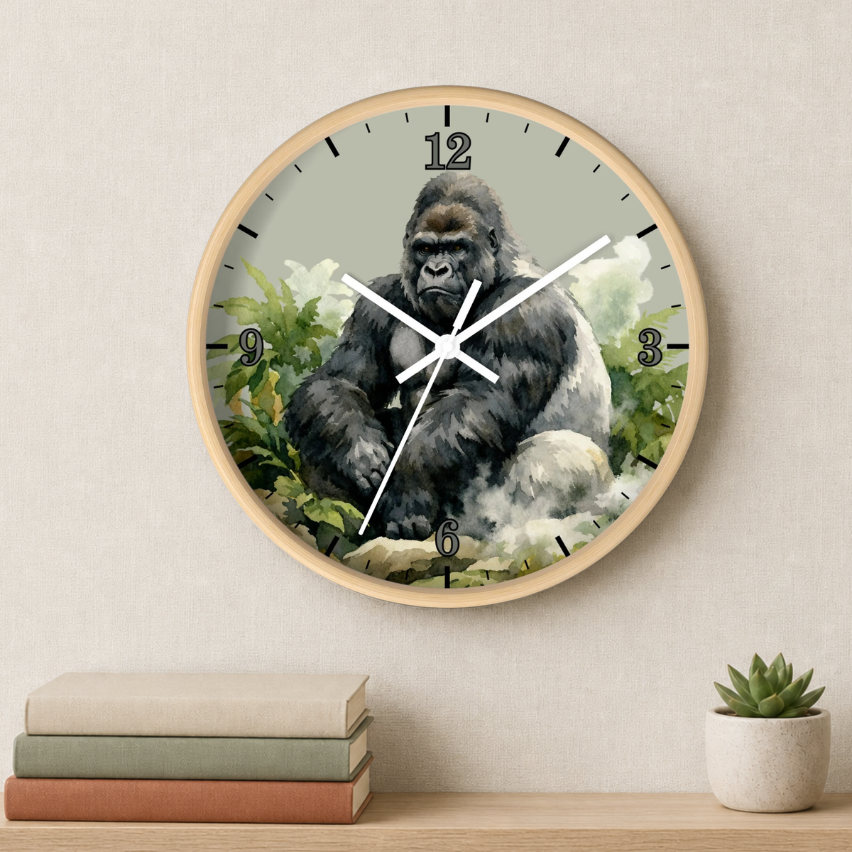 A round wall clock with a light wood frame hangs on a beige wall above a shelf with stacked books and a small potted succulent. The clock face features a detailed illustration of a gorilla in a natural setting.