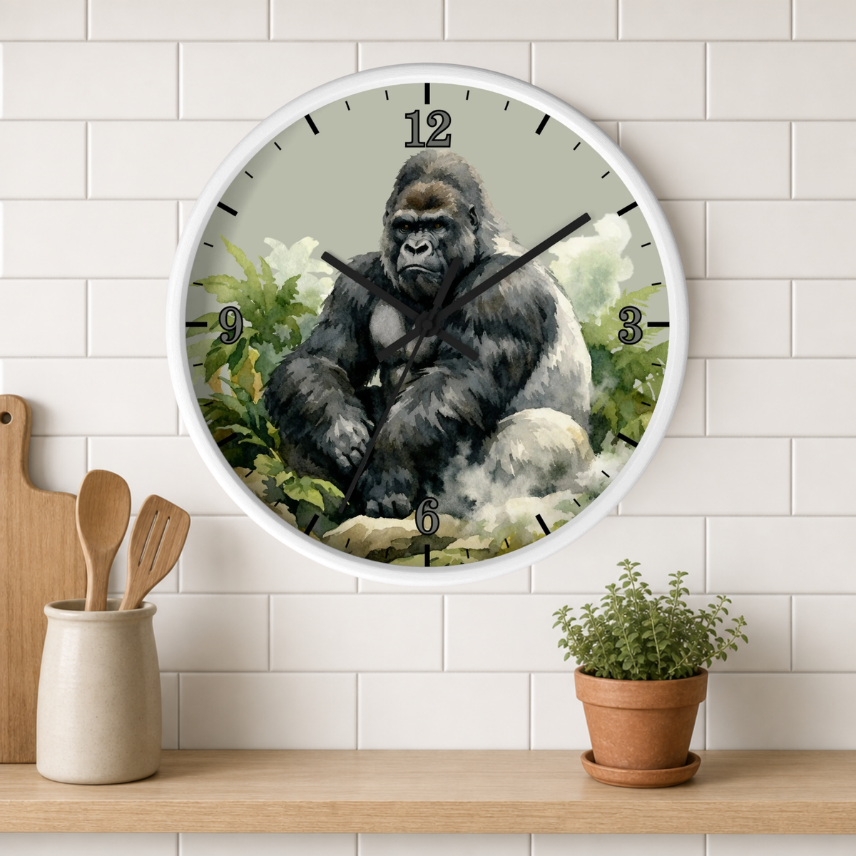 A round wall clock with a white frame hangs on a white subway tile wall above a wooden shelf. The clock face features a detailed illustration of a seated gorilla in green foliage.