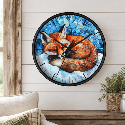 A round wall clock with a black frame and a printed illustration of a sleeping fox in blue and white tones, mounted on a white wood-paneled wall above a wooden table with a plant and part of a chair visible.