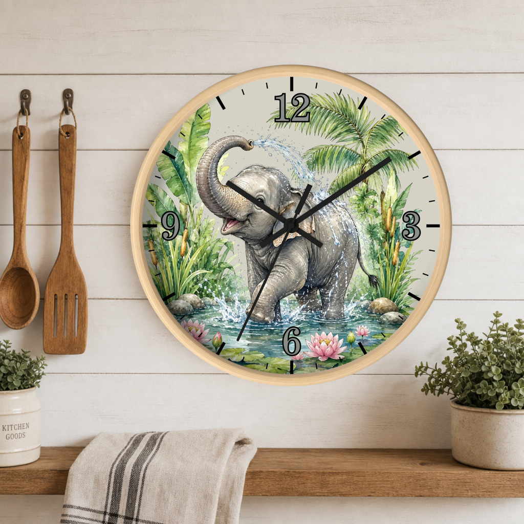 A round wall clock with a light wood frame hangs on a white wood-paneled wall above a shelf. The clock face features a colorful illustration of a gray elephant standing in water among green palm trees and lotus flowers.
