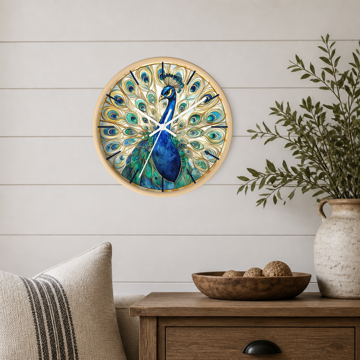 Round wall clock featuring a painted peacock with spread tail feathers in blue, teal, and gold tones, mounted on a white shiplap wall above a wooden side table with a plant and decorative bowl.