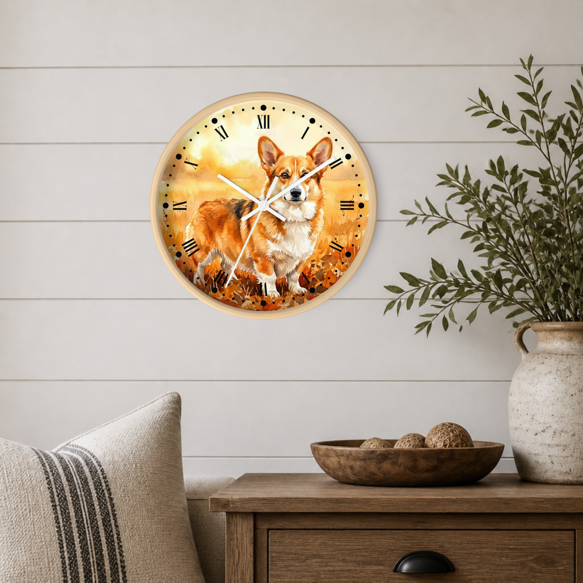 A round wall clock featuring a painted corgi on an autumn leaf background, mounted on a white shiplap wall above a wooden side table with a vase and bowl.