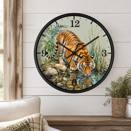 A round wall clock with a black frame and a printed illustration of a tiger drinking water, mounted on a white shiplap wall above a wooden shelf with a plant and part of a sofa visible.