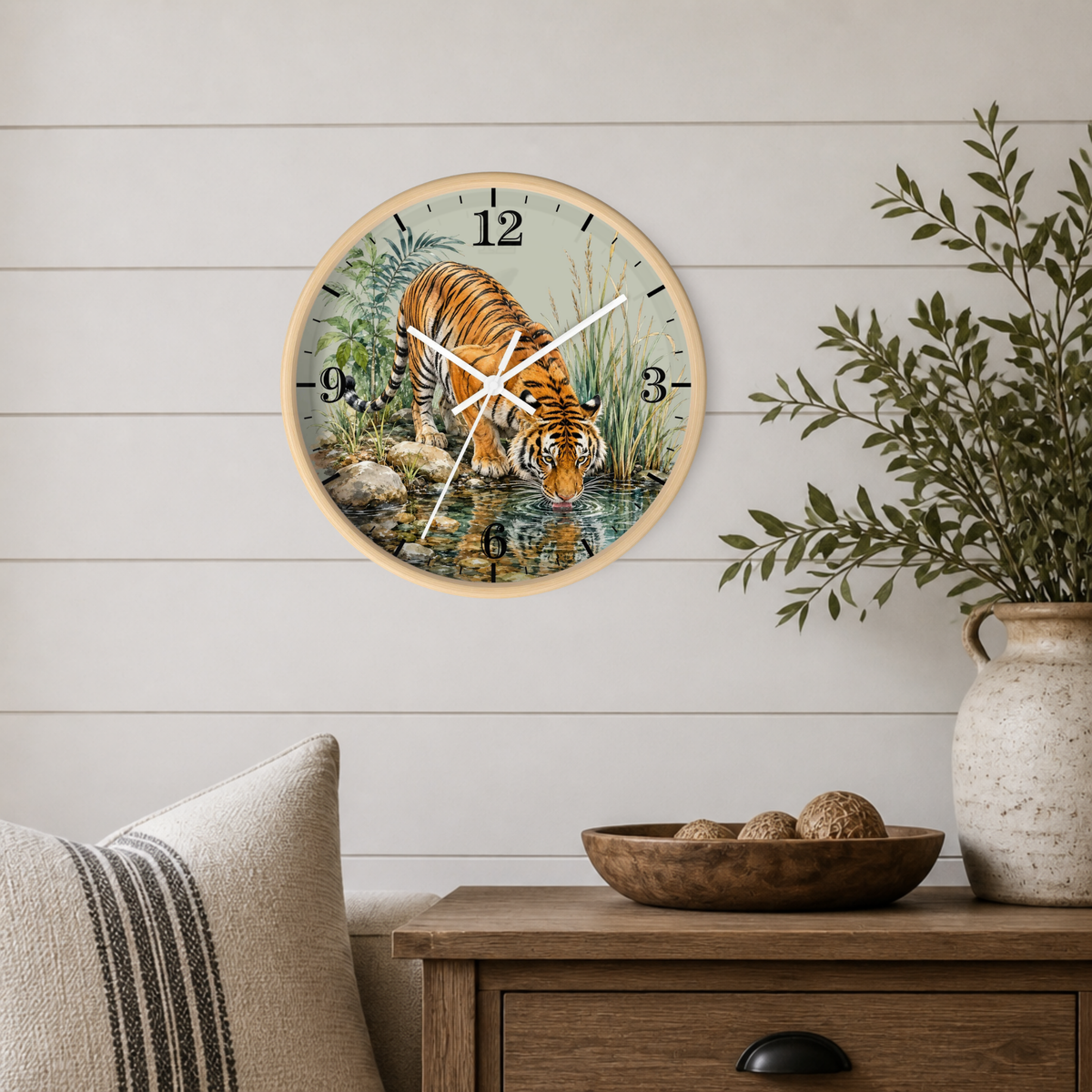 Round wall clock with a natural wood frame featuring a detailed illustration of a tiger drinking water, mounted on a white shiplap wall above a wooden side table with a plant and decorative bowl.