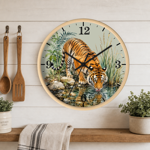 Round wall clock with a light wood frame featuring a detailed illustration of a tiger drinking water from a stream, mounted on a white wood paneled wall above a shelf with kitchen utensils and plants.