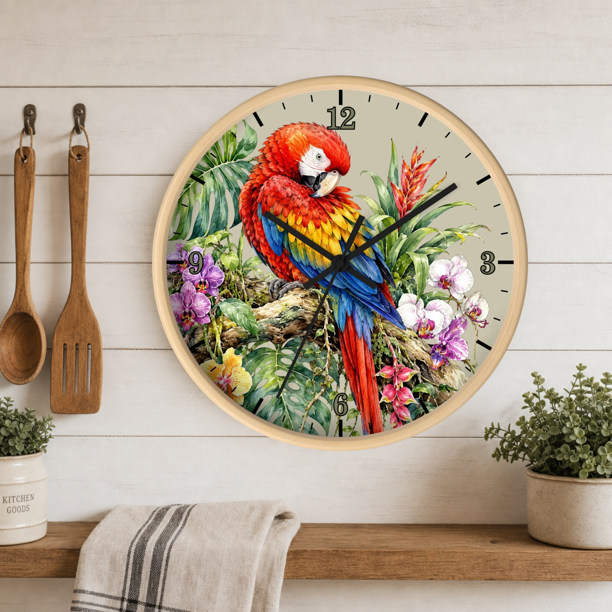 A round wall clock with a light wood frame hangs on a white wood-paneled wall above a shelf. The clock face features a vivid illustration of a red and blue parrot surrounded by tropical leaves and flowers.