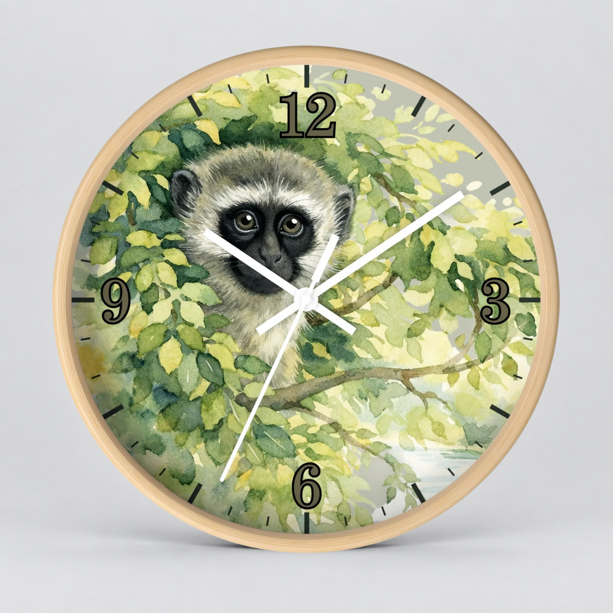 Round wall clock with a light wood frame and a printed dial featuring a vervet monkey face surrounded by green leaves. The clock has black Arabic numerals and white hands on a light gray background.