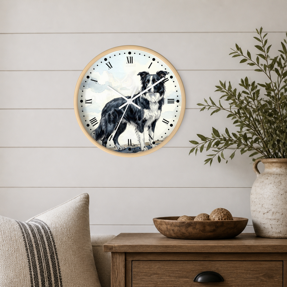 A round wall clock with a light wood frame hangs on a white shiplap wall above a wooden side table. The clock face features a black and white dog illustration over a soft blue sky background.