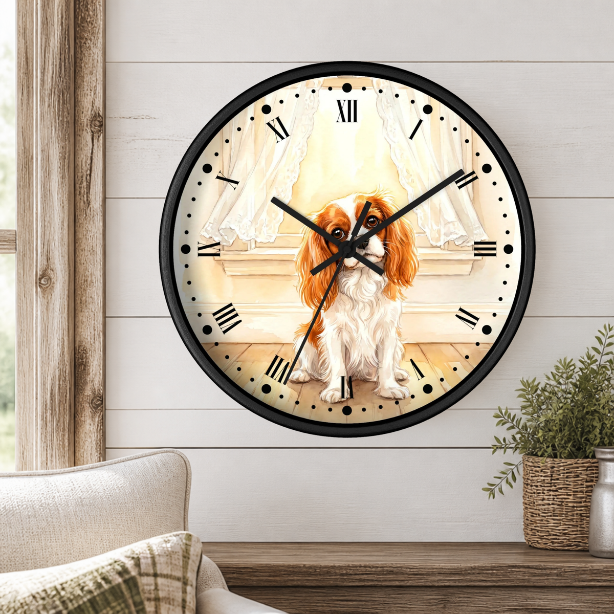 A round wall clock with a black frame and Roman numerals, featuring an illustration of a Cavalier King Charles Spaniel dog sitting in front of a window with curtains. The clock is mounted on a white shiplap wall above a wooden mantel with a small potted plant.