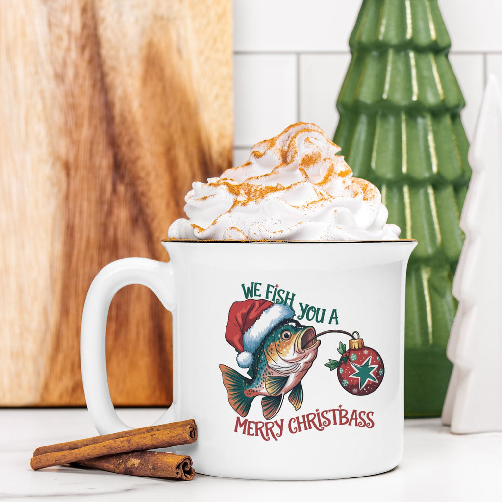 White mug with Christmas-themed design, filled with hot chocolate and whipped cream, on a wooden surface.