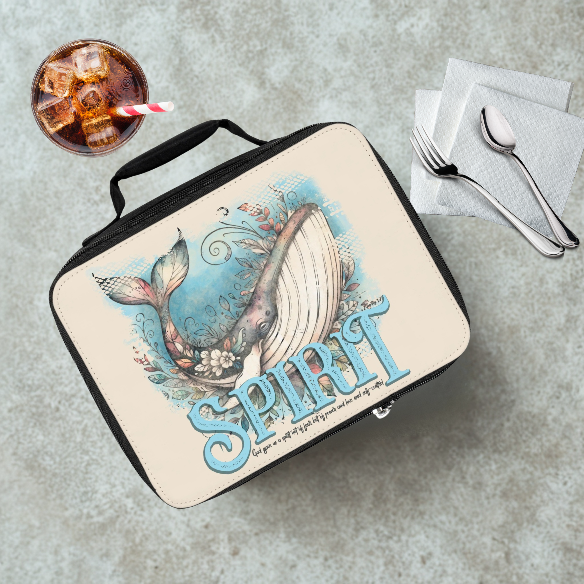 Lunch bag with whale design and 'Spirit' text on a concrete surface with a drink and utensils.