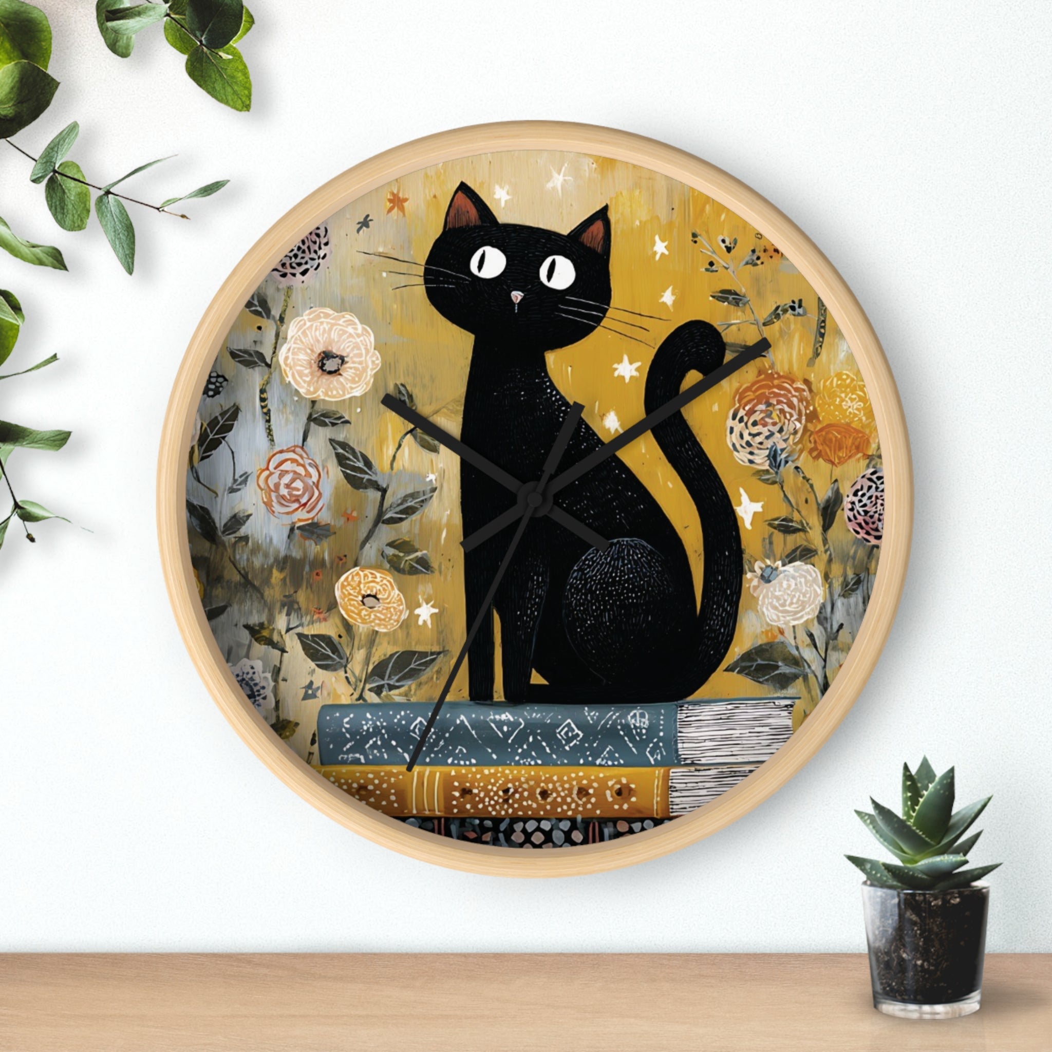 Decorative wall clock with a black cat design on a floral background, placed on a wooden surface with a plant.