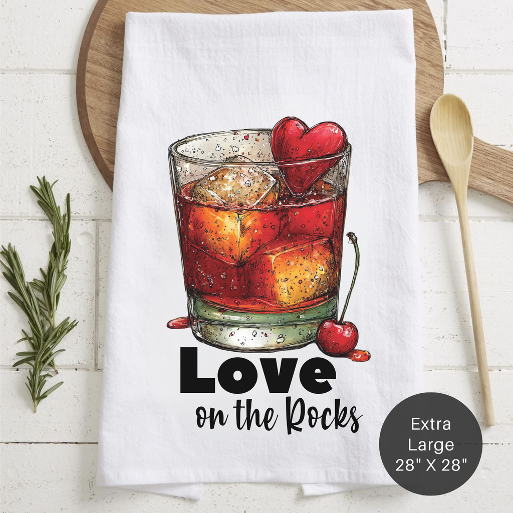 Tea towel with a cocktail graphic and 'Love on the Rocks' text, placed on a wooden surface.