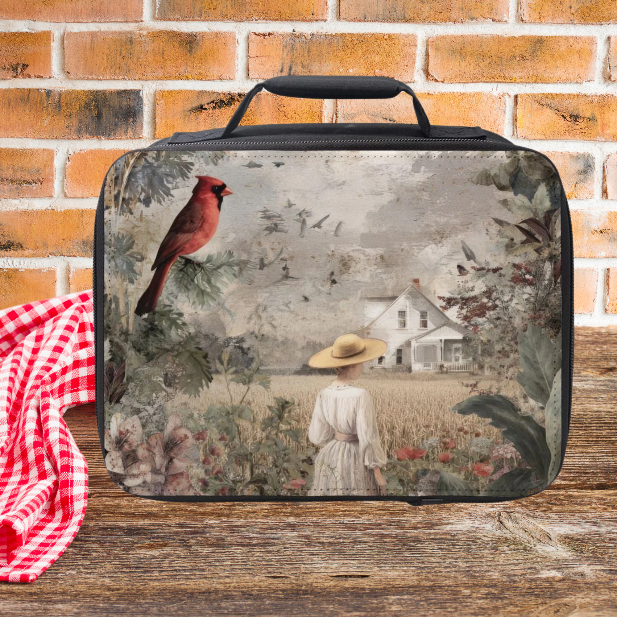 Rectangular fabric bag with a scenic design featuring a house, trees, and a person in a field on a wooden picnic table against a brick background.