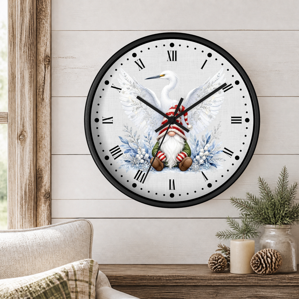 A round wall clock with a black frame and a white face featuring a white bird with wings spread, blue floral accents, and a gnome in a red-and-white striped Santa hat. The clock is mounted on a light wood shiplap wall above a wooden table with a candle, pinecones, and greenery in a styled interior setting.