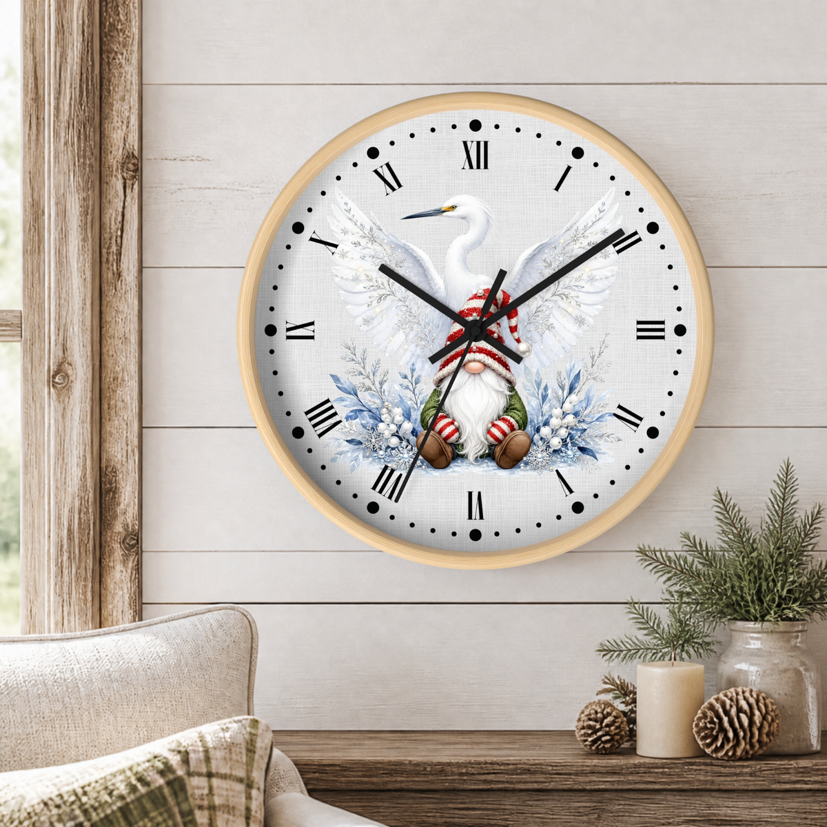 A round wall clock with a light wood frame hangs on a white shiplap wall above a rustic wooden table. The clock face features a white heron with outstretched wings, blue floral accents, and a red-and-white striped knit sweater.