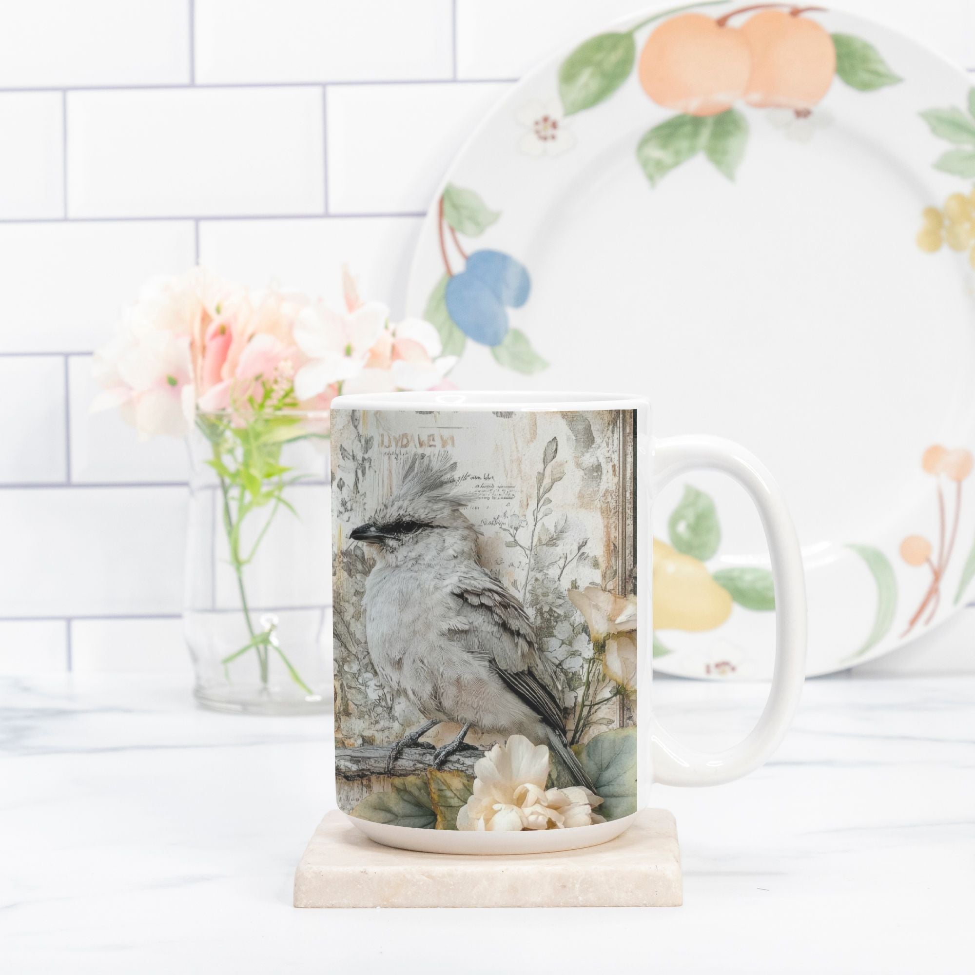 Mug with bird design on a marble coaster, next to a floral plate on a white tiled wall background.